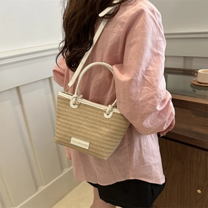French style woven straw bucket bag with white leather straps shown on a female model
