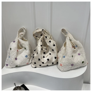 Détails de sacs cabas en tissu avec broderies florales et motifs cœurs sur socle ondulé