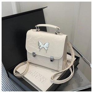 Detailed macro shot of a cream square bag featuring a silver liquid-effect butterfly buckle