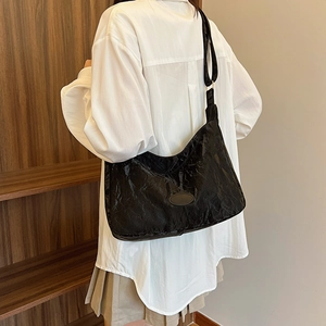 Chic black pleated hobo bag with a glossy finish and adjustable strap on model