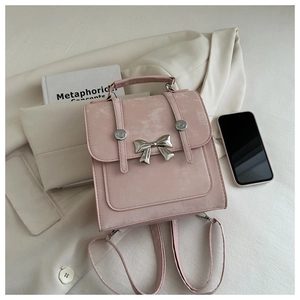 Detail of pink faux suede backpack featuring silver bow and metallic buckle on white blazer