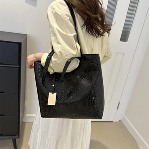 Large black crocodile pattern tote bag with gold tag shown on shoulder by model