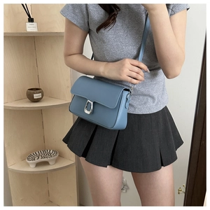 Sky blue crossbody bag with silver U-shaped lock shown on a model in a cozy indoor setting
