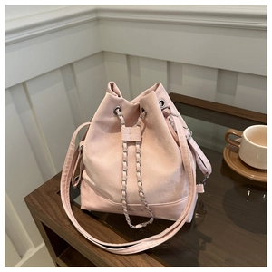 Pink drawstring bucket bag with silver chain detail placed on a wooden glass table