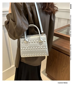 Detail of silver metallic quilted handbag with vertical stitching and smooth dual handles