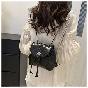 Detail of a black quilted leather mini backpack with silver chain straps on a model