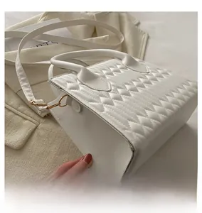 Detailed view of white quilted faux leather texture and gold hardware on small square bag