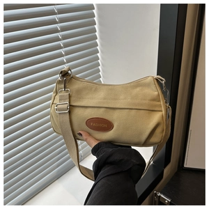 Detail view of khaki canvas crossbody bag with adjustable strap and oval fashion patch