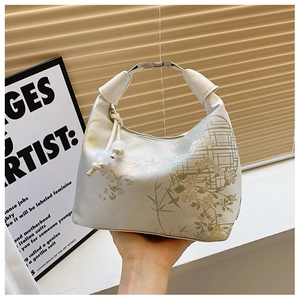 Detail of off-white handbag with floral patterns, metal handle, and pearl drawstring charm