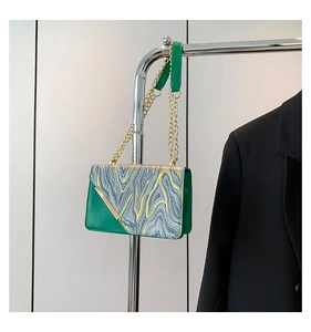 Dettaglio di pelle verde e motivo marmoreo con catena dorata su piccola borsa quadra