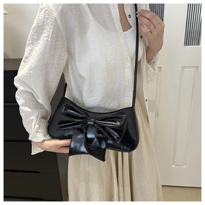 Detail of a black glossy shoulder bag with a large bow decoration and long strap