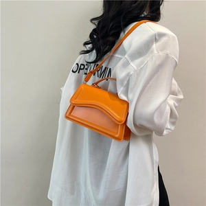Sac à bandoulière orange vif à rabat ondulé porté sur une chemise blanche chic
