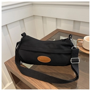 Detail of minimalist black canvas crescent bag with fashion leather patch on a wood table