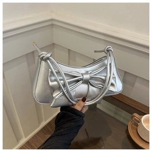 Detail of silver metallic shoulder bag with large bow and knot straps in a lifestyle setting