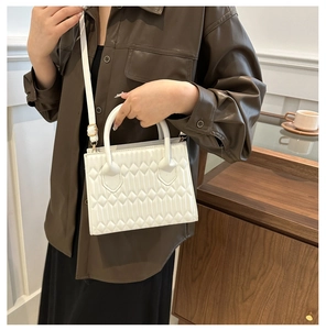 Detailed view of white quilted crossbody bag with gold hardware and cylindrical handle