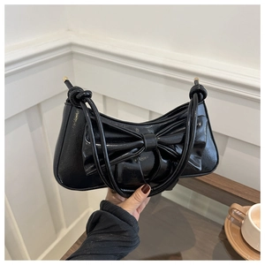 Detail of a black patent leather underarm bag with a large bow and glossy finish