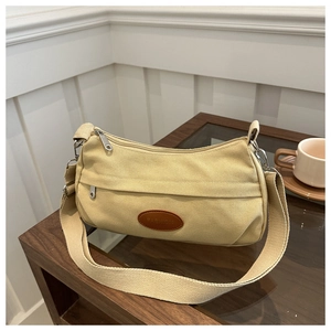 Detail of khaki canvas shoulder bag with brown leather patch and wide strap on wood table