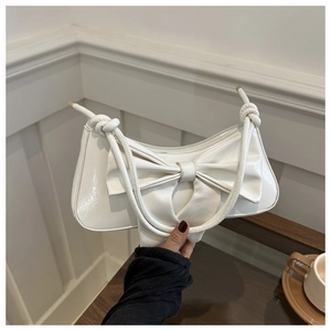 Detail of white glossy leather handbag with large bow and knotted shoulder strap