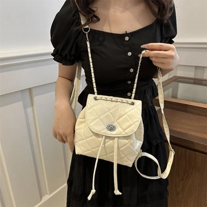 Quilted beige mini backpack with metal chain strap worn by a model in casual style