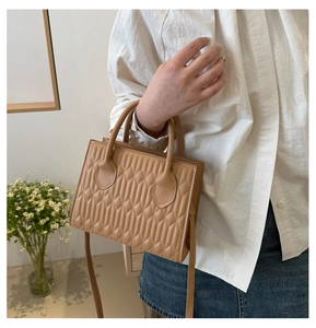 Detail of tan quilted leather handbag with crossbody strap and double round handles