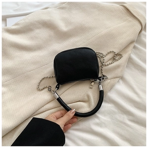 Detail of black litchi texture mini handbag with silver bead chain on beige corduroy