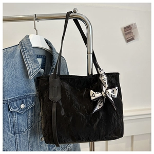 Close-up of black tote bag with unique pleated texture and fashion scarf handle detail