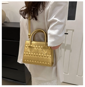 Detail of gold quilted small tote bag with metallic finish and metal hardware on shoulder