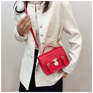 Chic red retro messenger bag with gold hardware worn over a stylish white tweed jacket