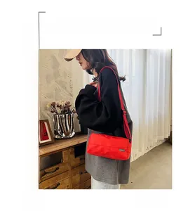 Detail of red nylon cylinder crossbody bag featuring green woven label and wide strap