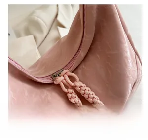 Close-up of smooth pink zipper and woven rope pullers on textured crossbody handbag