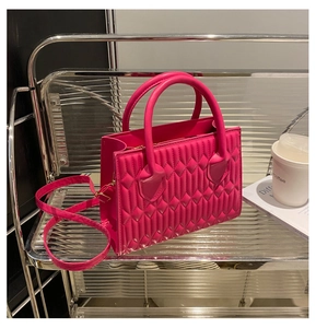 Detailed view of rose red quilted crossbody bag with dual top handles and long strap