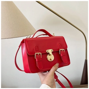 Detail of red vintage messenger bag with gold buckles and adjustable strap in hand