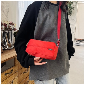 Detail of red nylon shoulder bag with adjustable strap and green woven label