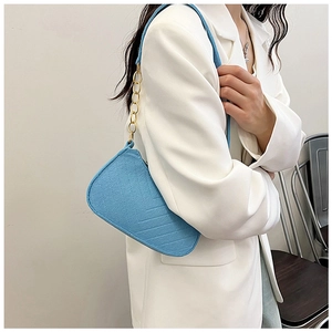 Detail of light blue felt baguette bag with geometric texture and gold chain strap