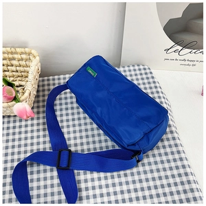 Detail of royal blue nylon crossbody bag featuring an adjustable strap and green logo label