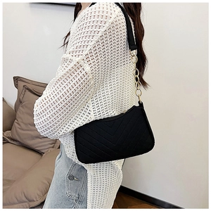 Model wearing a black quilted felt baguette bag with gold chain strap detail