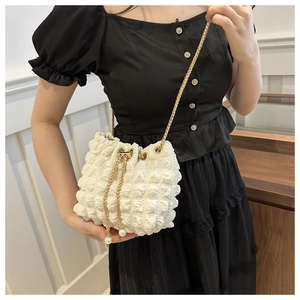 Detail of white popcorn texture bucket bag with pearl drawstring and gold chain strap