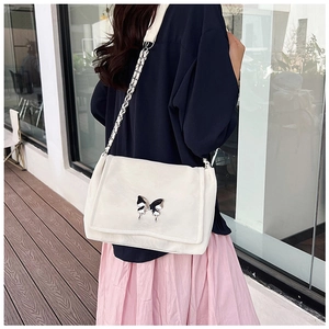 Detailed view of white leather shoulder bag with silver butterfly buckle on model