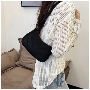 Detail view of black quilted faux leather shoulder bag with golden rings and V-pattern