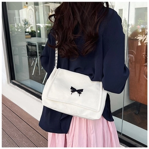 Detail of white PU leather shoulder bag featuring a black butterfly bow and chain strap