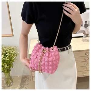 Pink bubble texture bucket bag with gold chain and pearl drawstring details shown indoors
