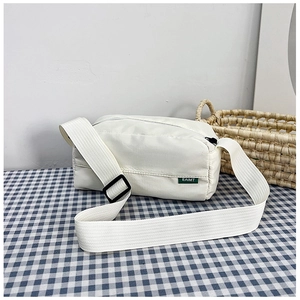 Detail showing the white nylon crossbody bag's green label and wide fabric shoulder strap