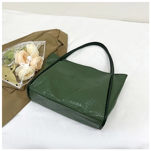 Detail of dark green woven tote bag with slim black straps on elegant white background