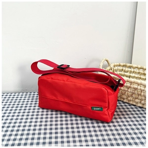Detail of red nylon crossbody bag with wide strap and brand label on checkered cloth