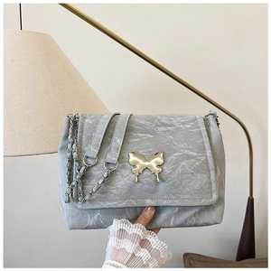 Detail of grey textured shoulder bag featuring a decorative butterfly metallic clasp