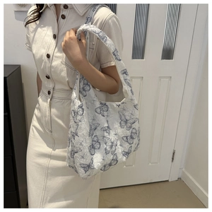 Détail du sac à bandoulière en peluche avec imprimé papillon bleu porté par un mannequin