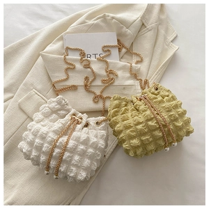 Detail of popcorn texture bucket bag with gold chain strap and pearl drawstring charms