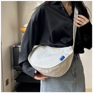 Gros plan d'un sac demi-lune en toile blanche avec étiquette bleue et large bandoulière
