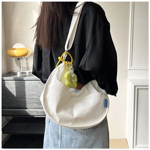 Détail du sac bandoulière demi-lune en toile blanche avec breloque fleur jaune et étiquette