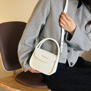 Sac bandoulière blanc minimaliste avec poignée incurvée et bandoulière porté par le mannequin